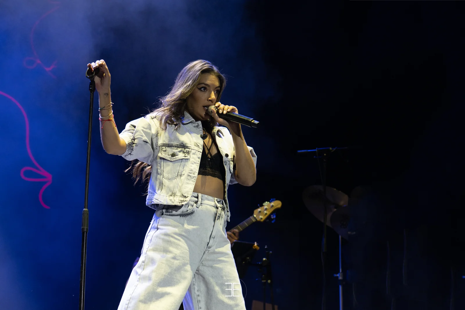 Ana Guerra canta ante el micrófono de pie bajo una luz azul, con el bajista desenfocado detrás