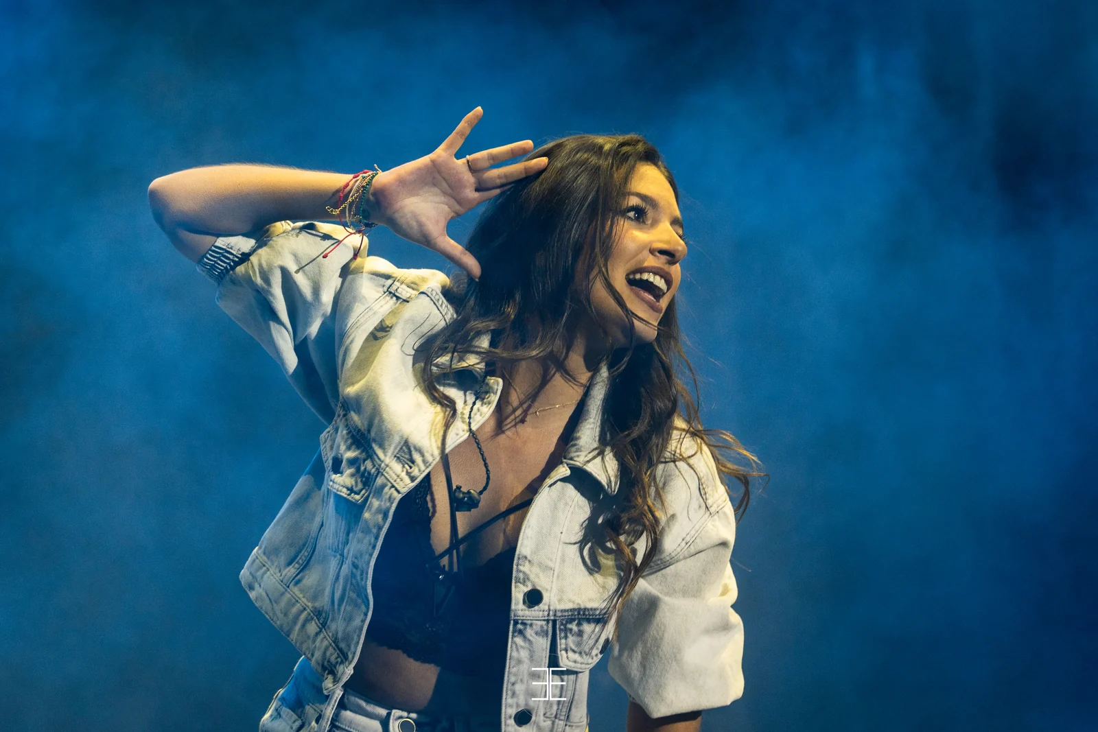 Ana Guerra se lleva una mano a la frente mientras canta, con el pelo suelto sobre un fondo azul