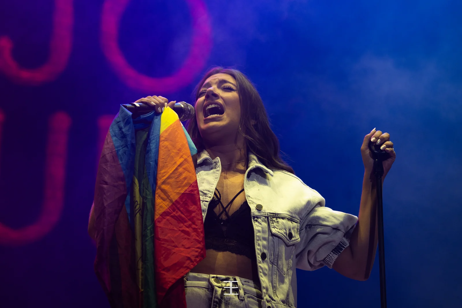 Ana Guerra canta con la bandera arcoíris sobre el hombro, con el neón rojo desenfocado detrás