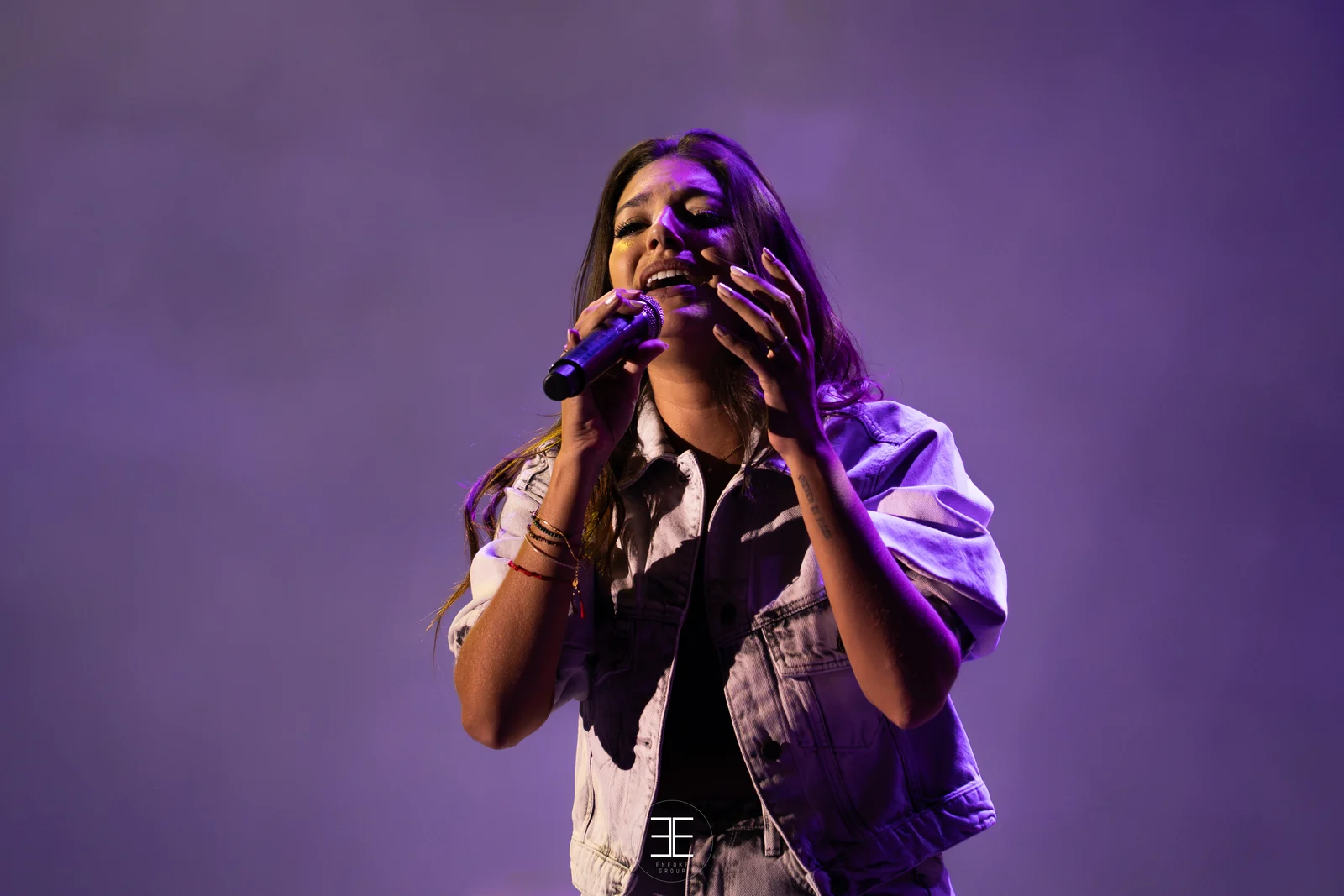 Primer plano de Ana Guerra cantando con las dos manos en el micrófono bajo una luz morada