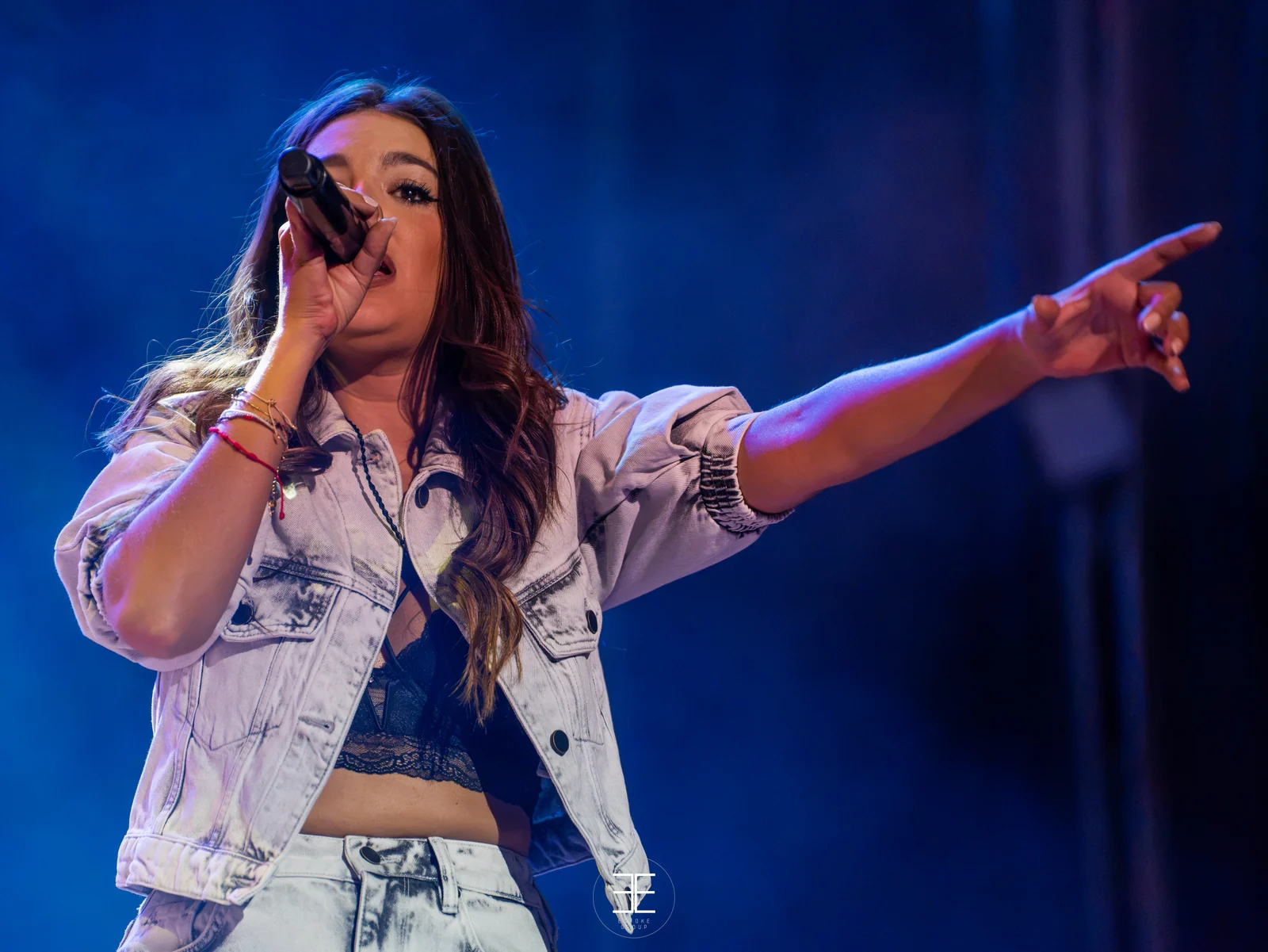 Ana Guerra canta señalando al público con el brazo estirado, sobre un fondo azul intenso