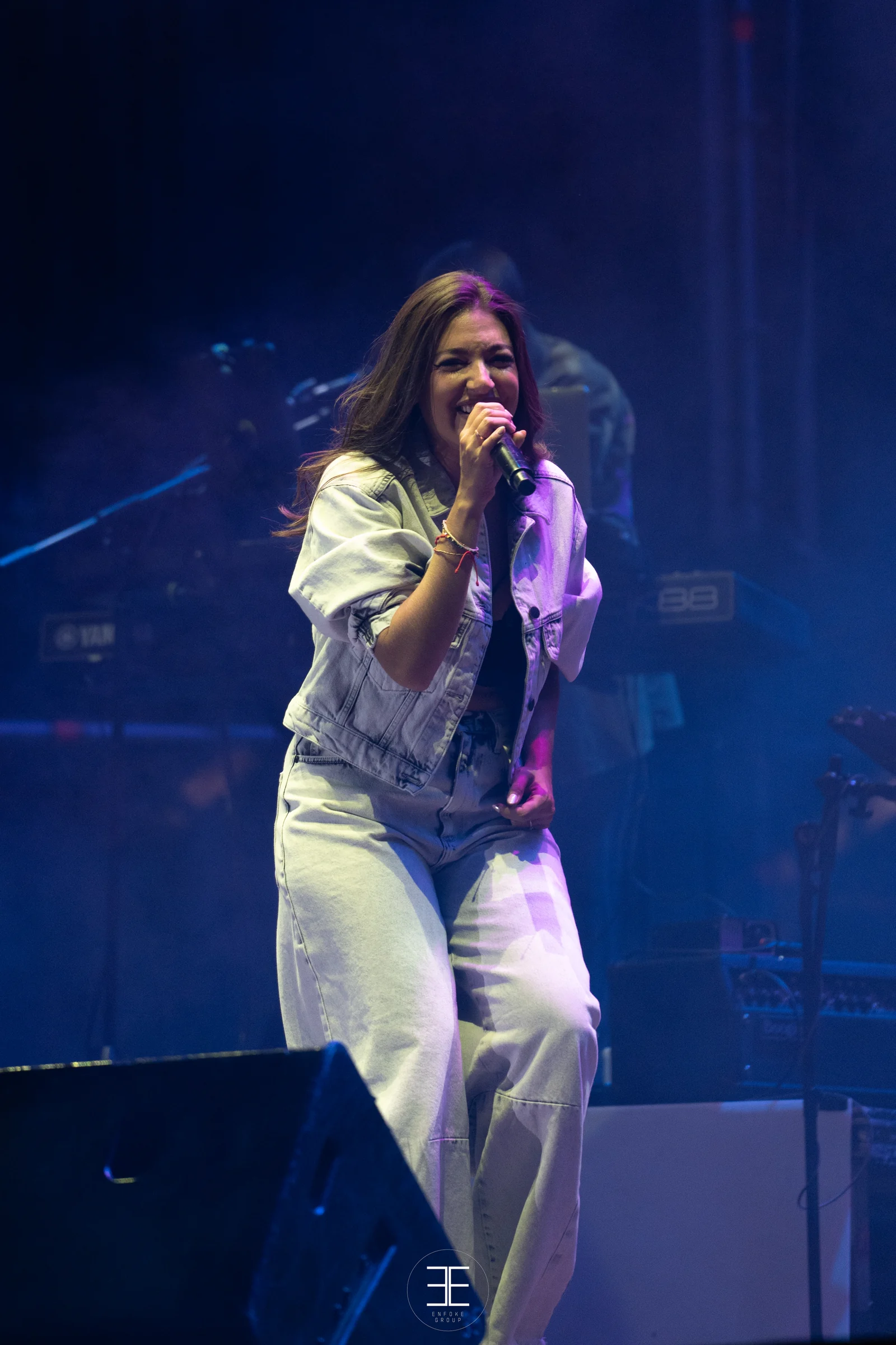 Ana Guerra, de cuerpo entero y en vertical, canta sobre un fondo azul con los monitores a sus pies