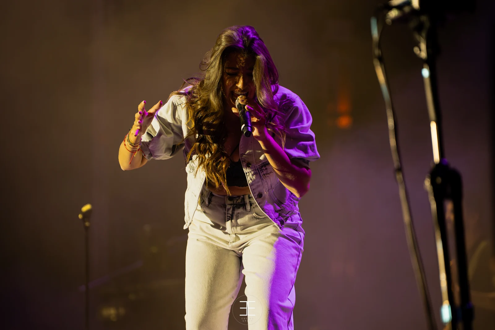 Ana Guerra canta con las dos manos levantadas, iluminada de naranja y morado