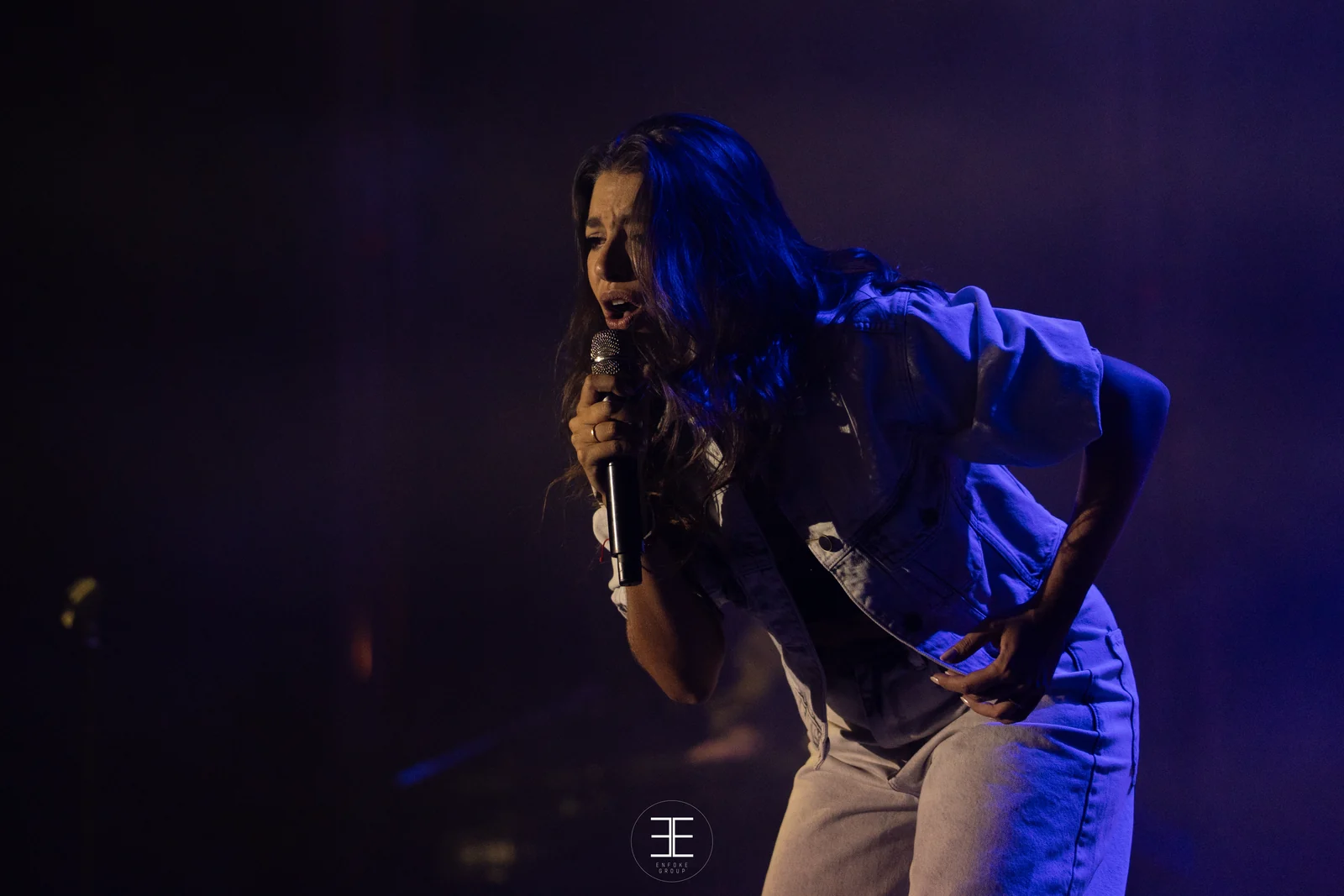 Ana Guerra canta inclinada hacia delante, entre luces azules y rosas