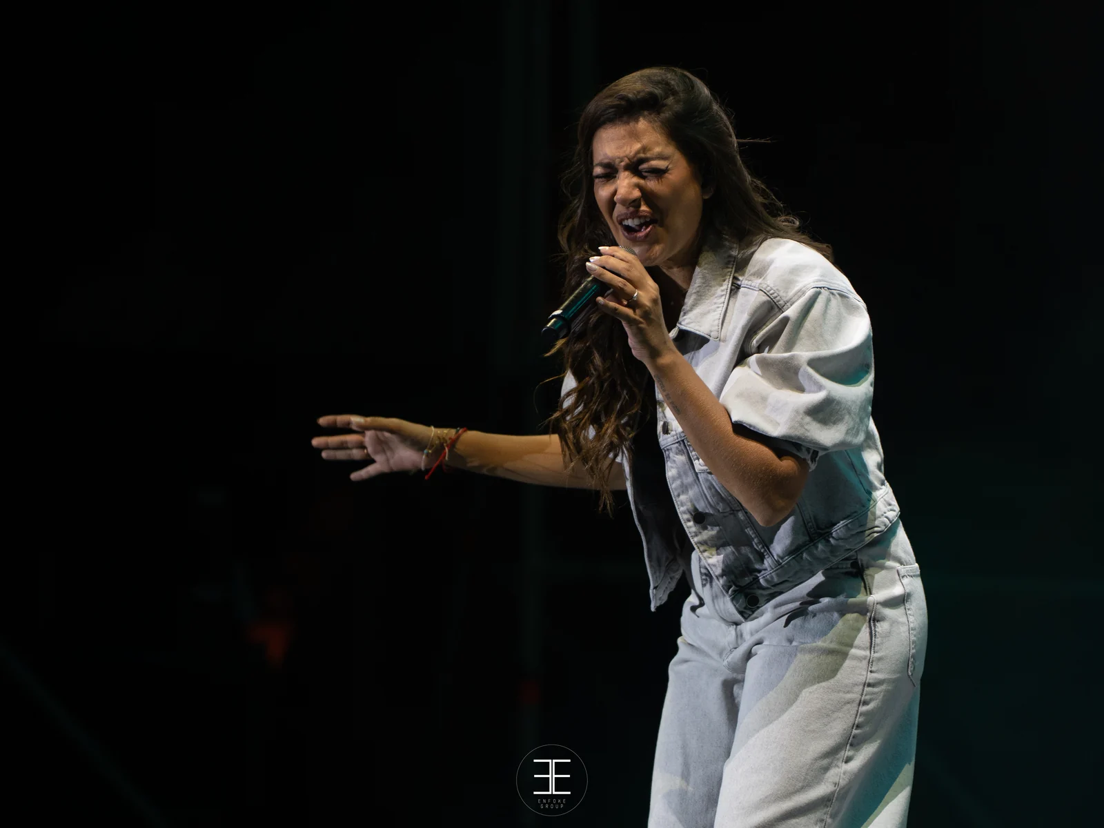 Ana Guerra canta con el brazo extendido hacia el público, recortada por un foco sobre fondo negro