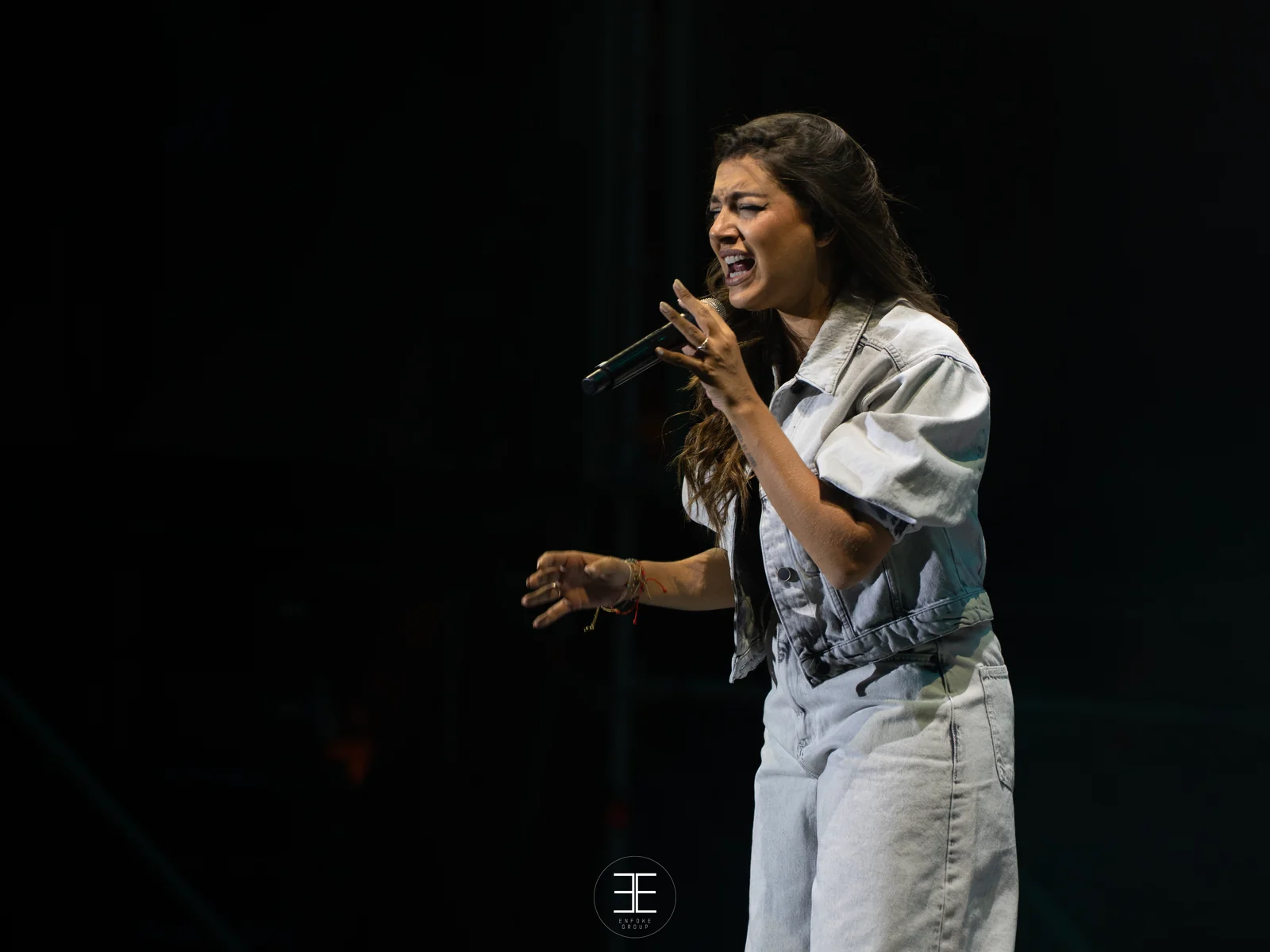 Ana Guerra canta con el brazo hacia delante y la cara tensa, sobre el negro del escenario