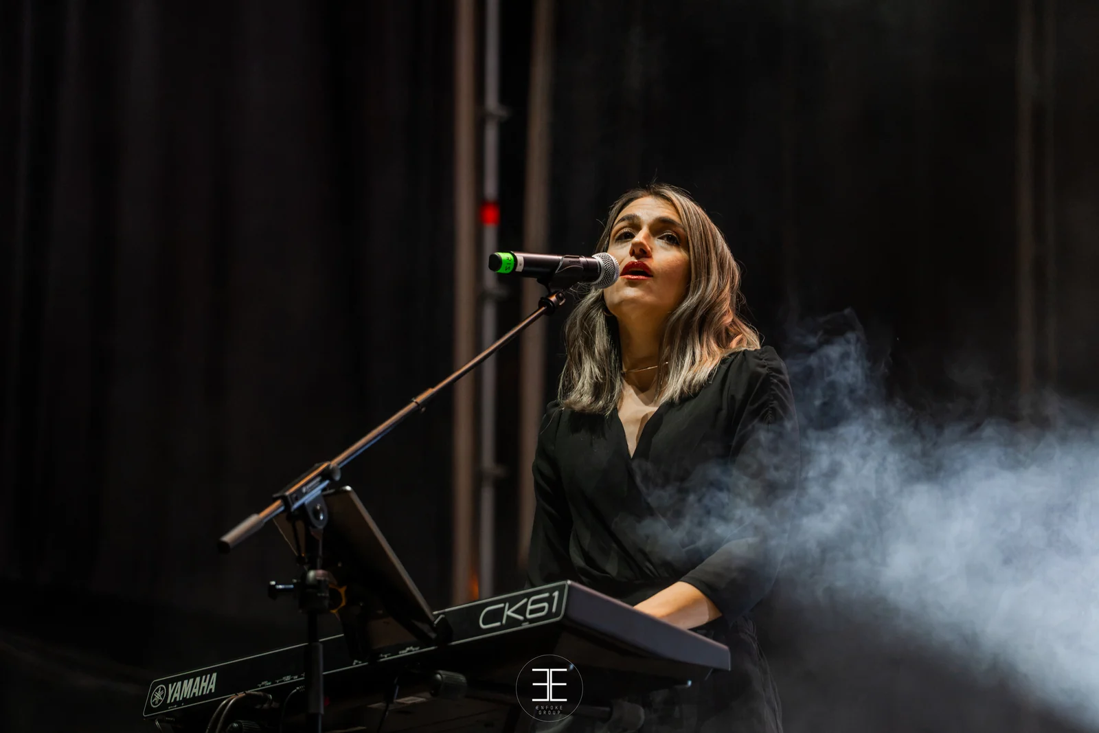 La teclista canta inclinada sobre el teclado mientras el humo le pasa por delante