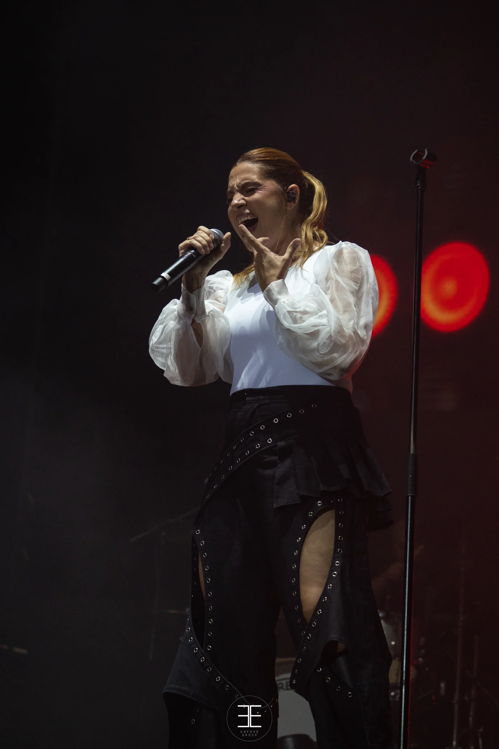Leire Martínez canta con el micrófono de mano, recortada por una luz roja a su derecha