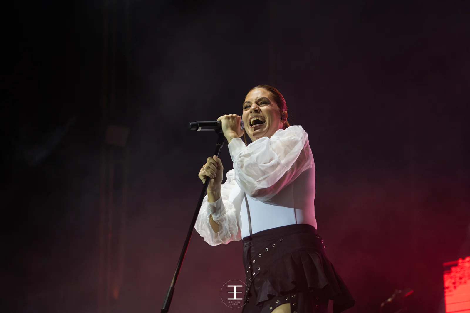 Leire Martínez canta agarrada al pie del micrófono sobre un fondo rojo y magenta