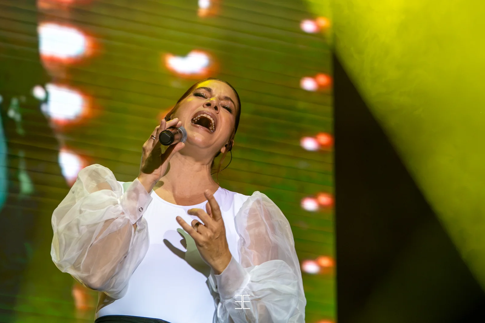 Leire Martínez canta con el micrófono de mano ante la pantalla encendida en verde y amarillo