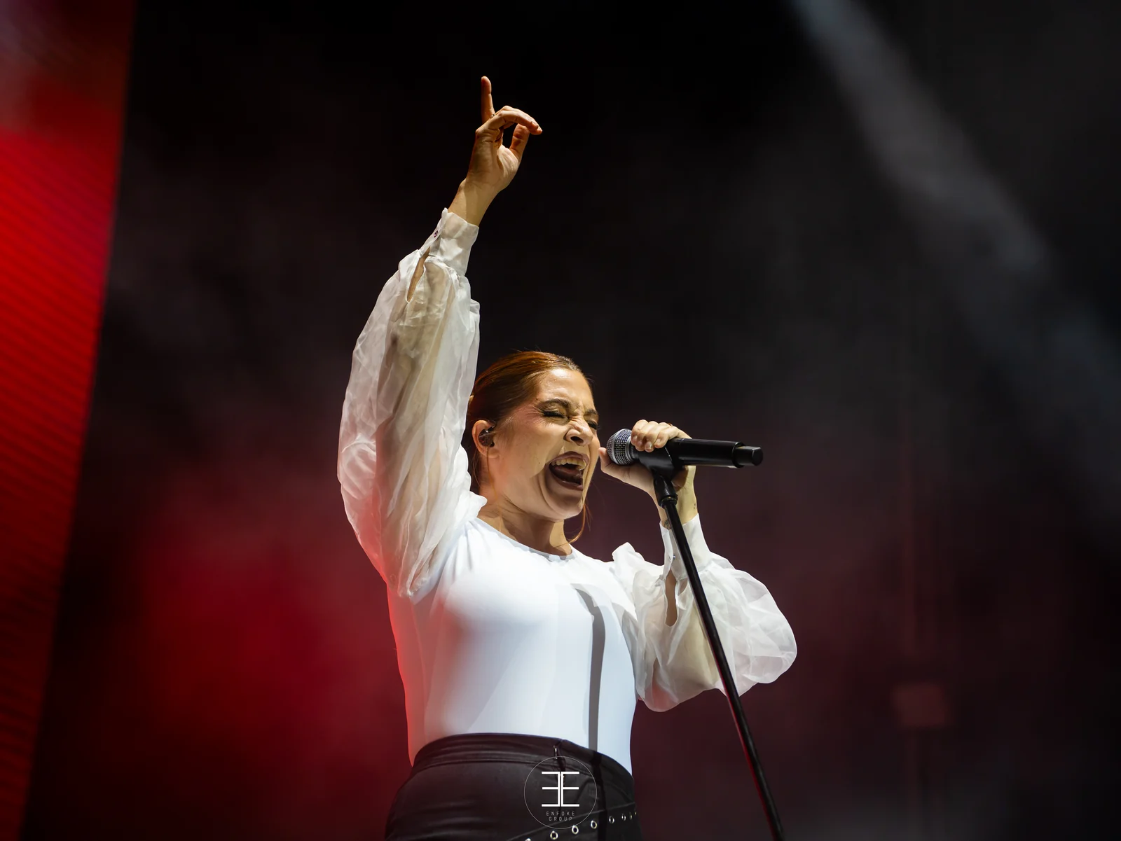 Leire Martínez canta señalando hacia arriba con el dedo índice, sobre un fondo rojo y negro
