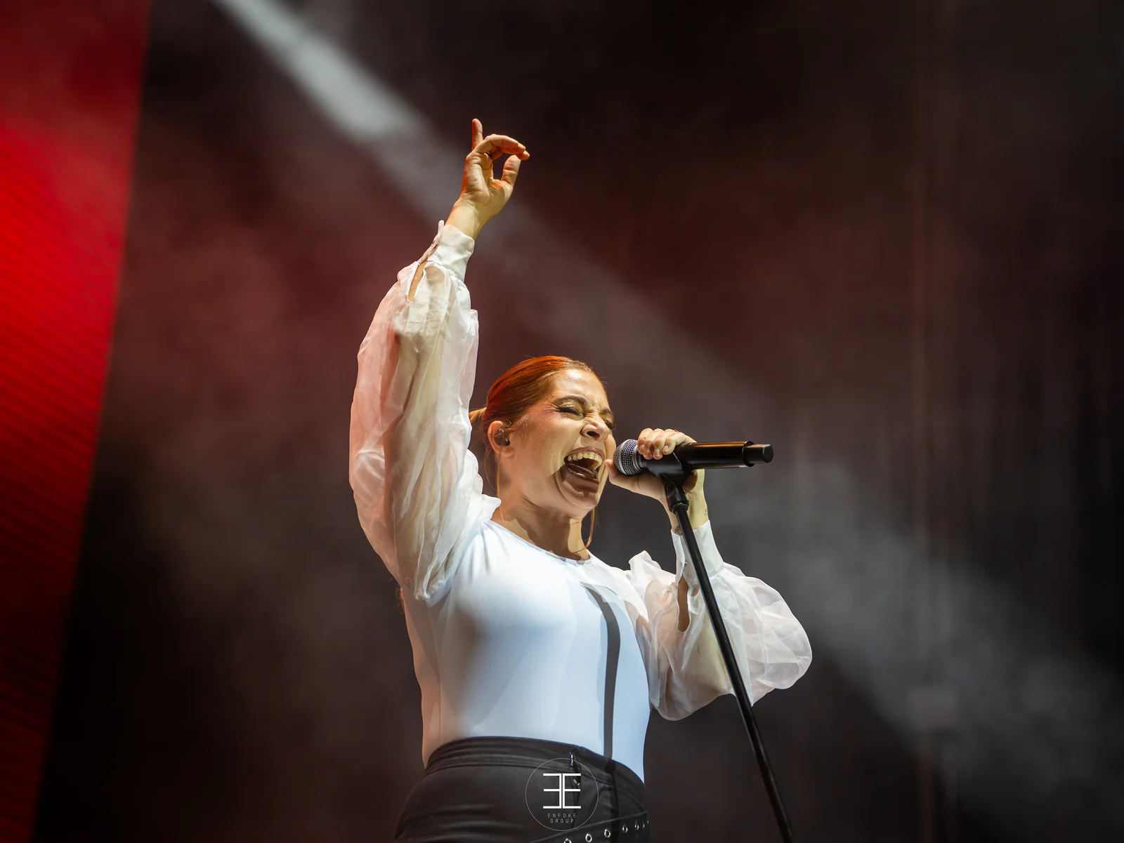 Leire Martínez canta con el brazo en alto, cruzada por las franjas de luz del escenario