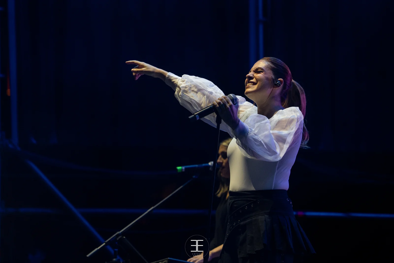 Leire Martínez señala al público con el brazo estirado, sobre un fondo azul