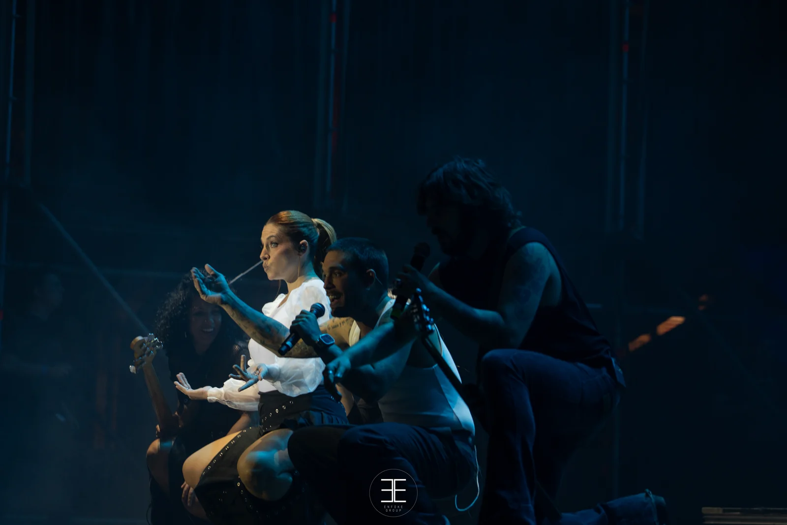 La banda al completo agachada en corro sobre el escenario, entre luces azules