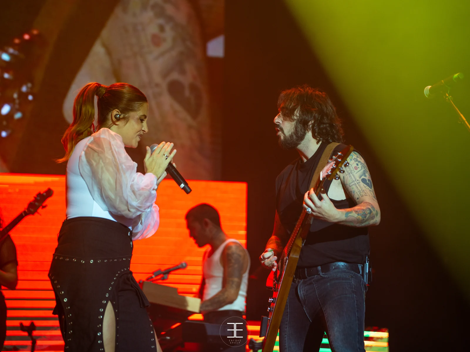 Leire Martínez y el guitarrista, frente a frente, ante una pantalla llena de corazones