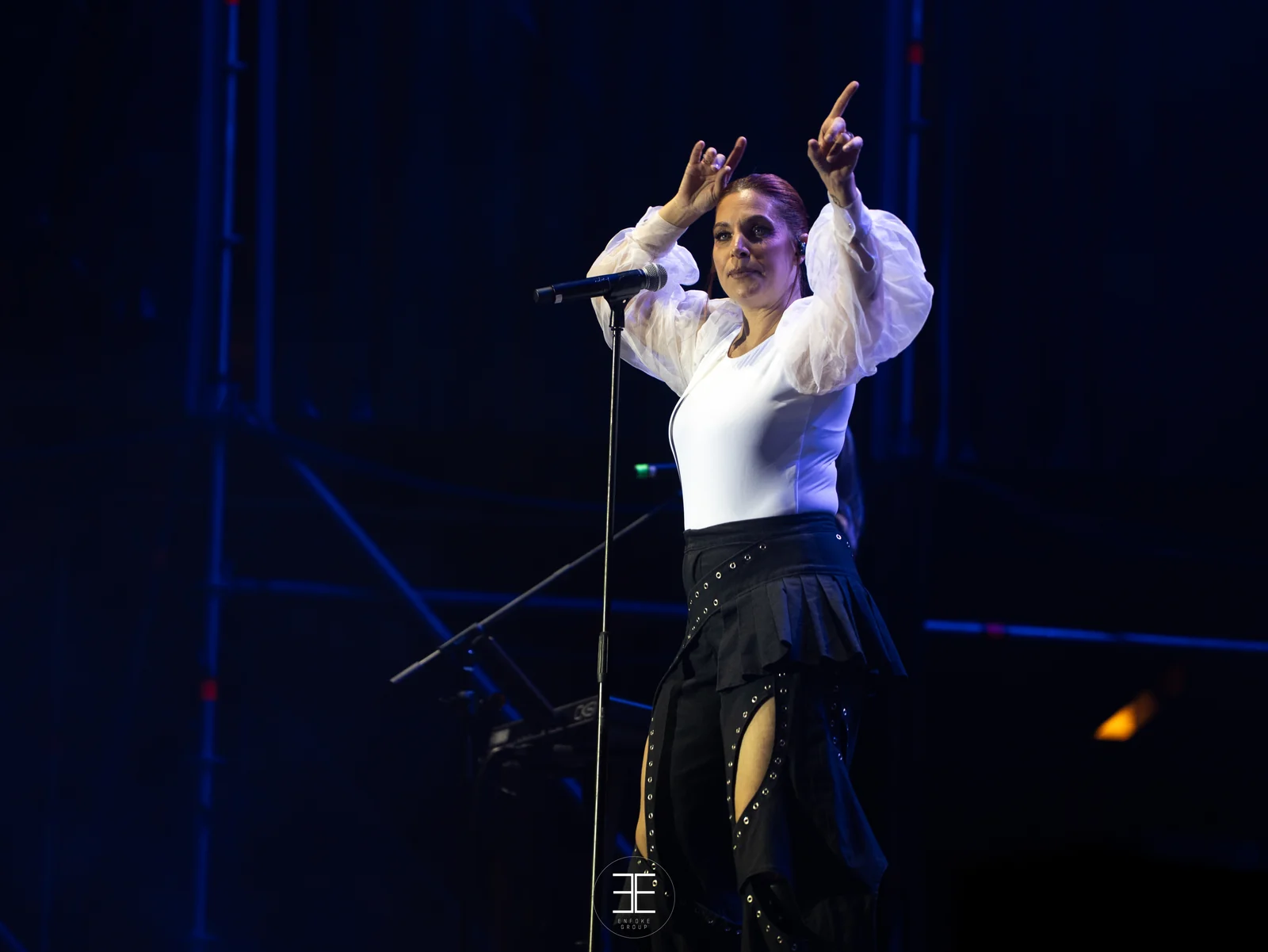 Leire Martínez levanta las dos manos cantando bajo una luz azul
