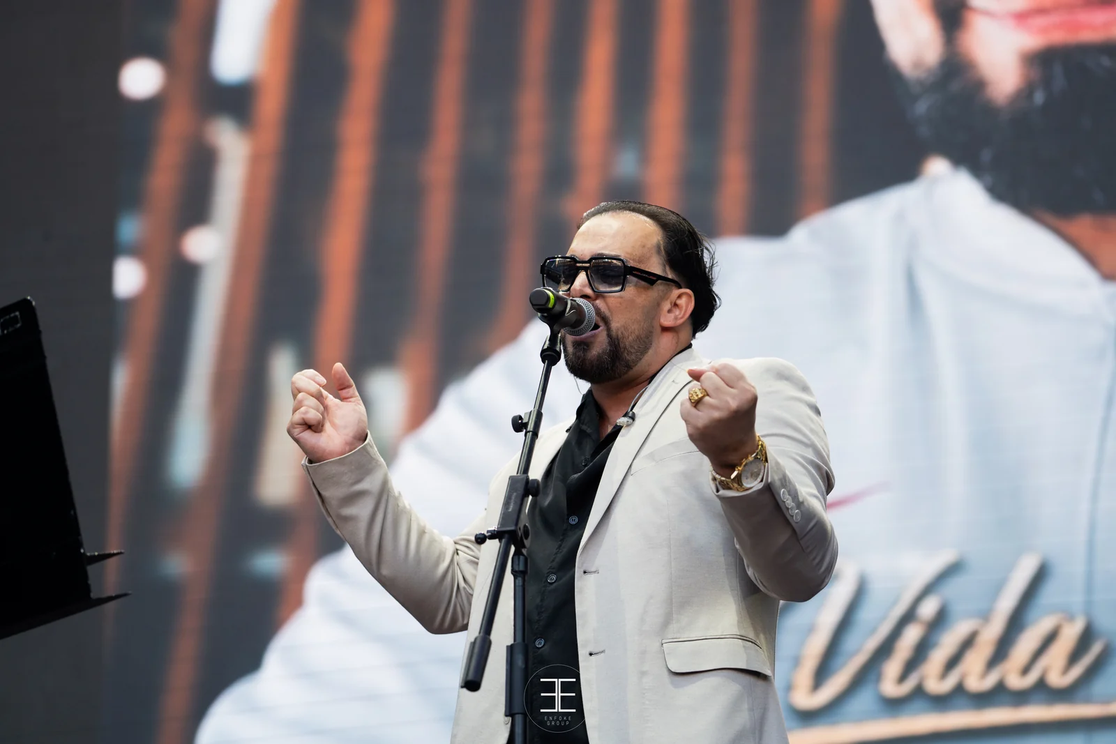 El Pérrez canta al micro de pie con gafas de sol y americana clara, los dos puños cerrados a la altura del pecho