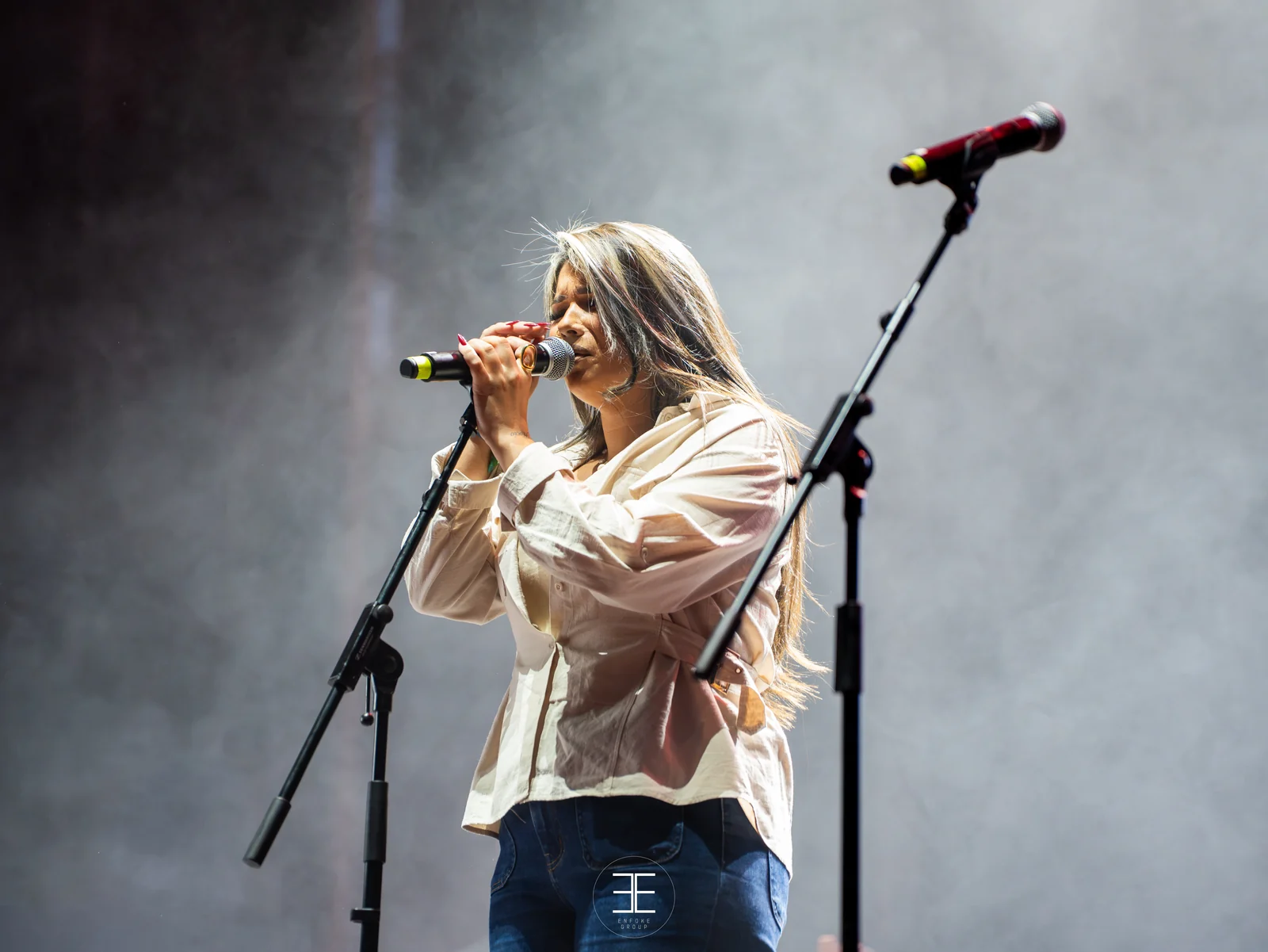 Una mujer canta con micro de mano entre dos pies de micro, con humo de escena detrás