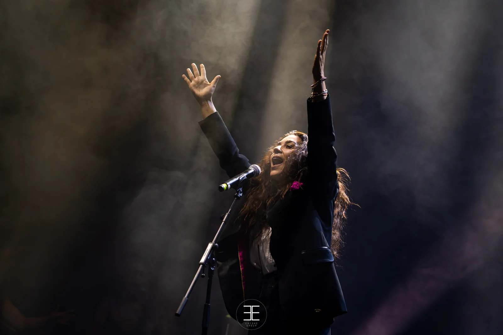 Sandra Carrasco con los dos brazos levantados sobre la cabeza mientras canta, recortada contra el humo del escenario