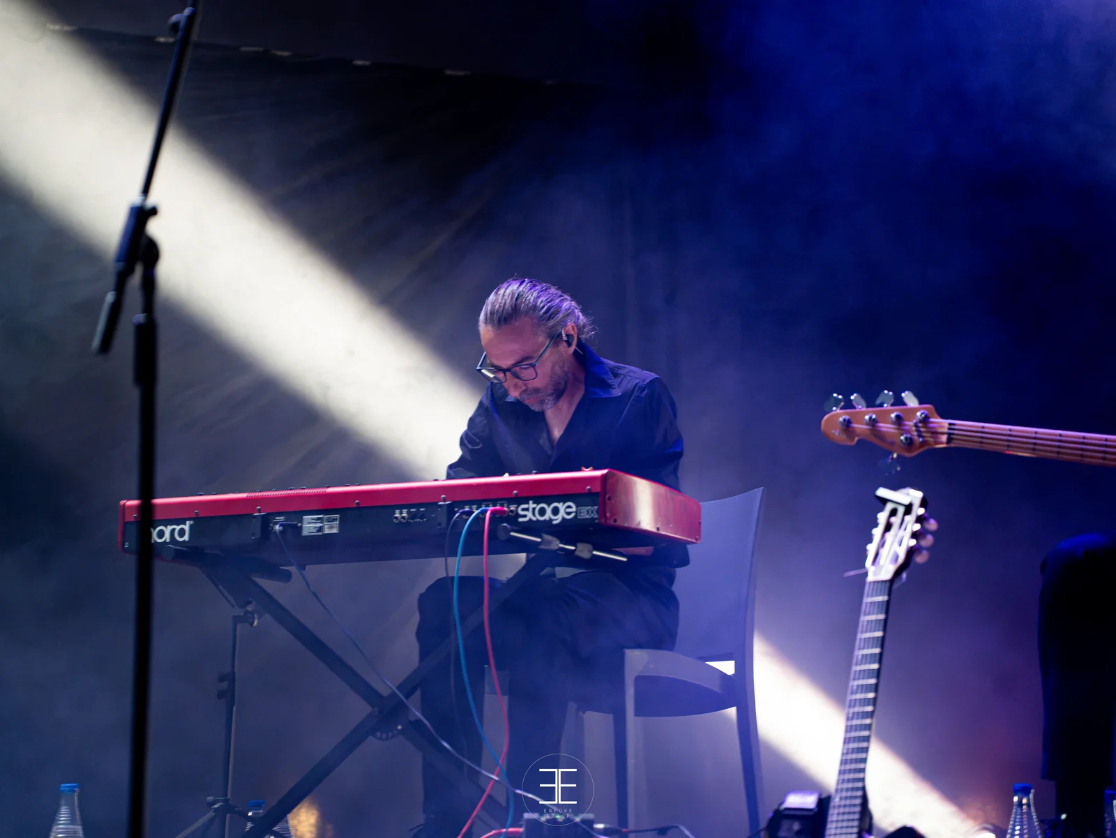 El pianista, con gafas y auricular, tocando un teclado rojo; a su derecha, un bajo eléctrico esperando en el soporte