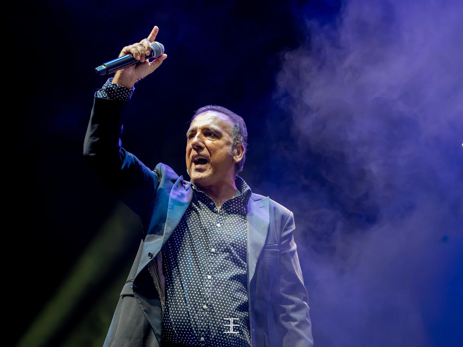 Enrique Heredia «Negri» con el micrófono alzado por encima de la cabeza, cantando con la boca abierta y el brazo extendido