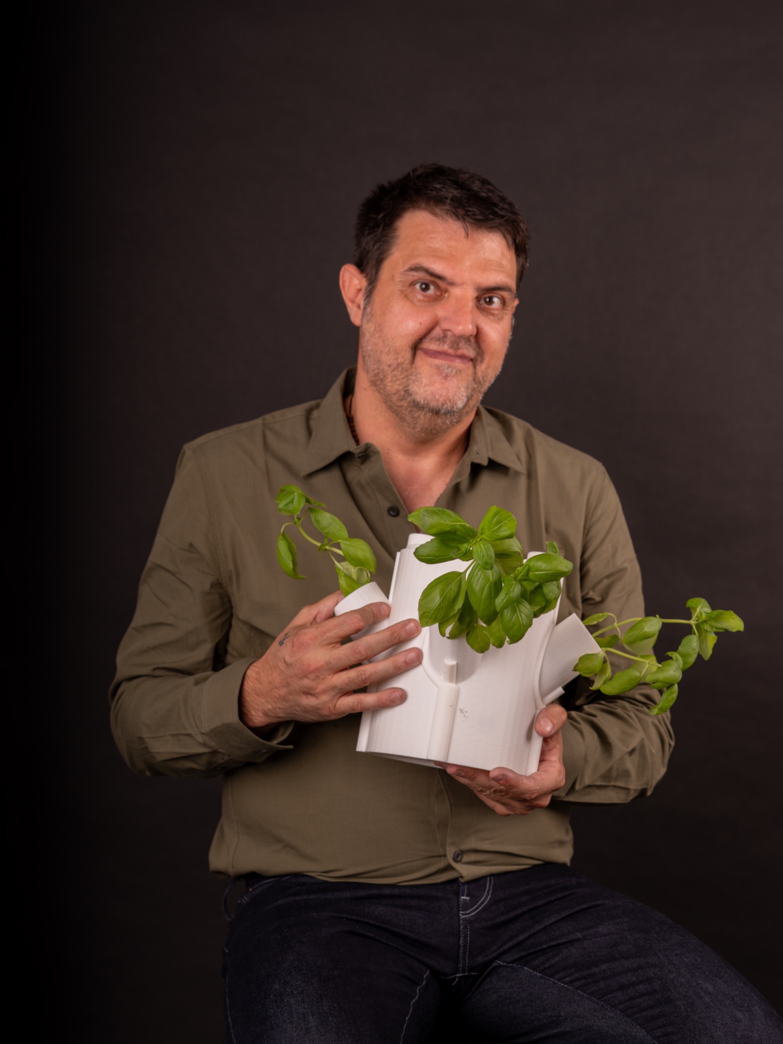 Fernando Fernández Martínez con camisa verde oliva sosteniendo una pieza blanca de la torre de cultivo con una planta