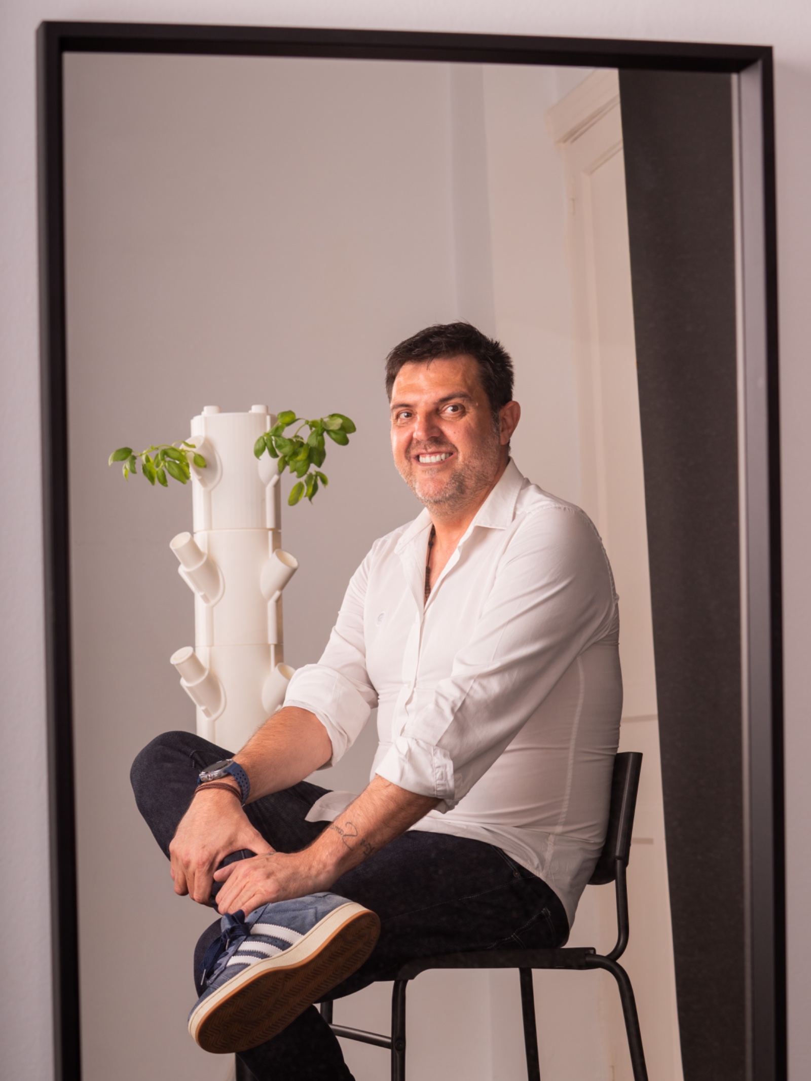 Fernando Fernández Martínez con camisa blanca, sentado junto a una torre de cultivo, reflejado en un espejo de marco negro
