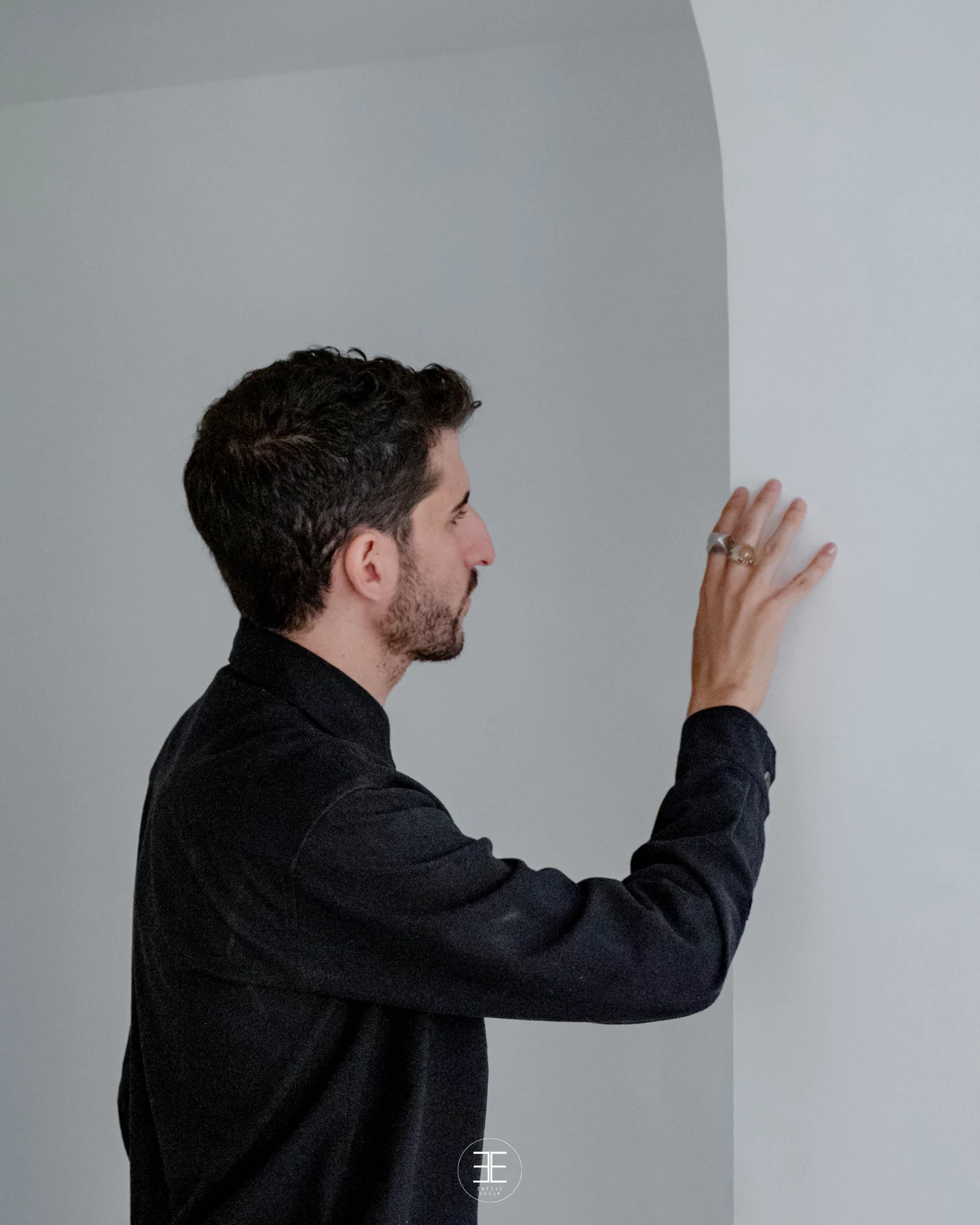 Raúl Almenara de perfil, con la mano abierta apoyada en la pared blanca junto a un arco