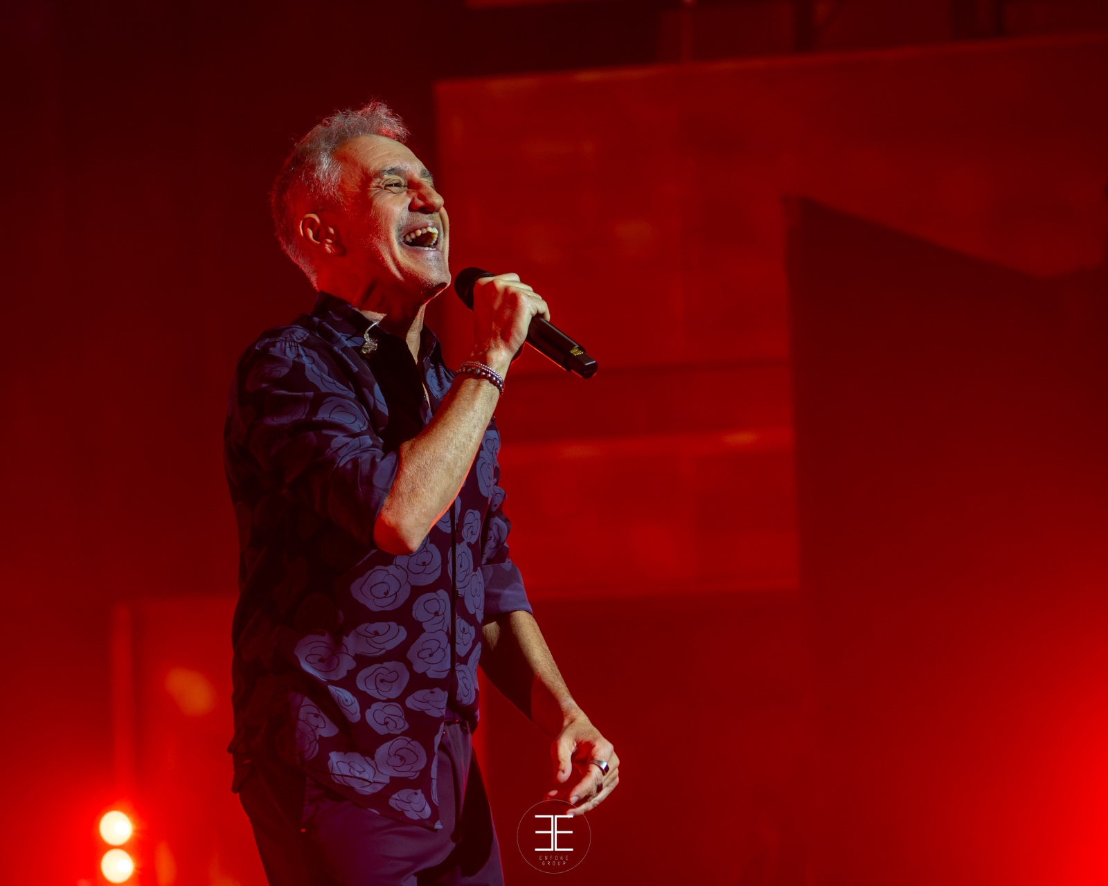 Sergio Dalma sonríe mientras canta, con el escenario teñido de rojo